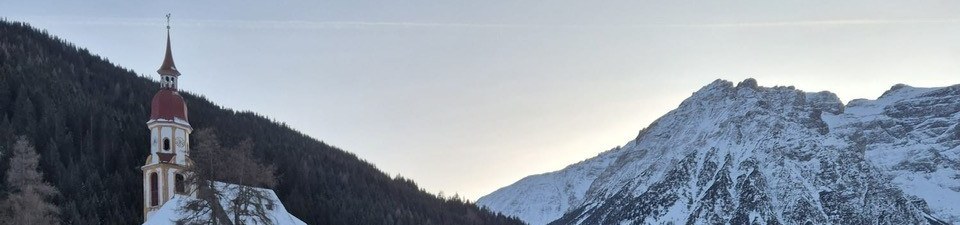 Kirchturm von St. Nikolaus vor den verschneiten Bergen