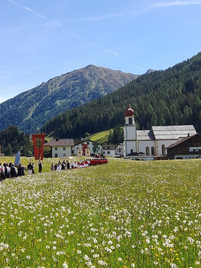 Pfarrkirche St. Josef in Schmirn mit Zwiebelturm, davor eine blühende Wiese