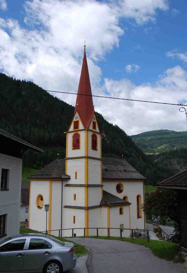 Pfarrkirche St. Jodok mit rotem Spitzturm vor den Bergen